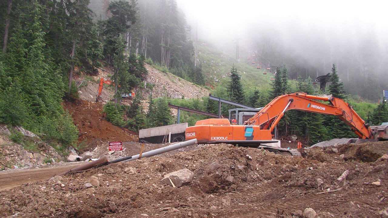 A large orange and black excavator on top of a hill.