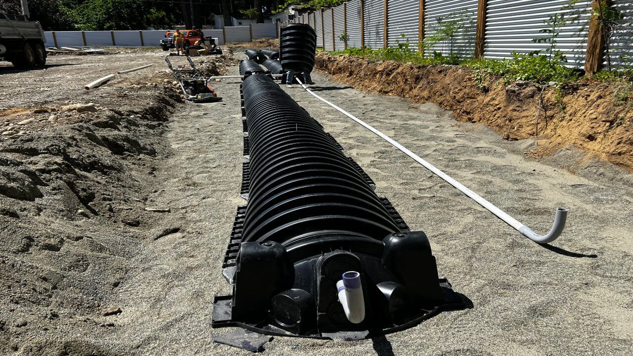 A black pipe laying on the ground next to a fence.