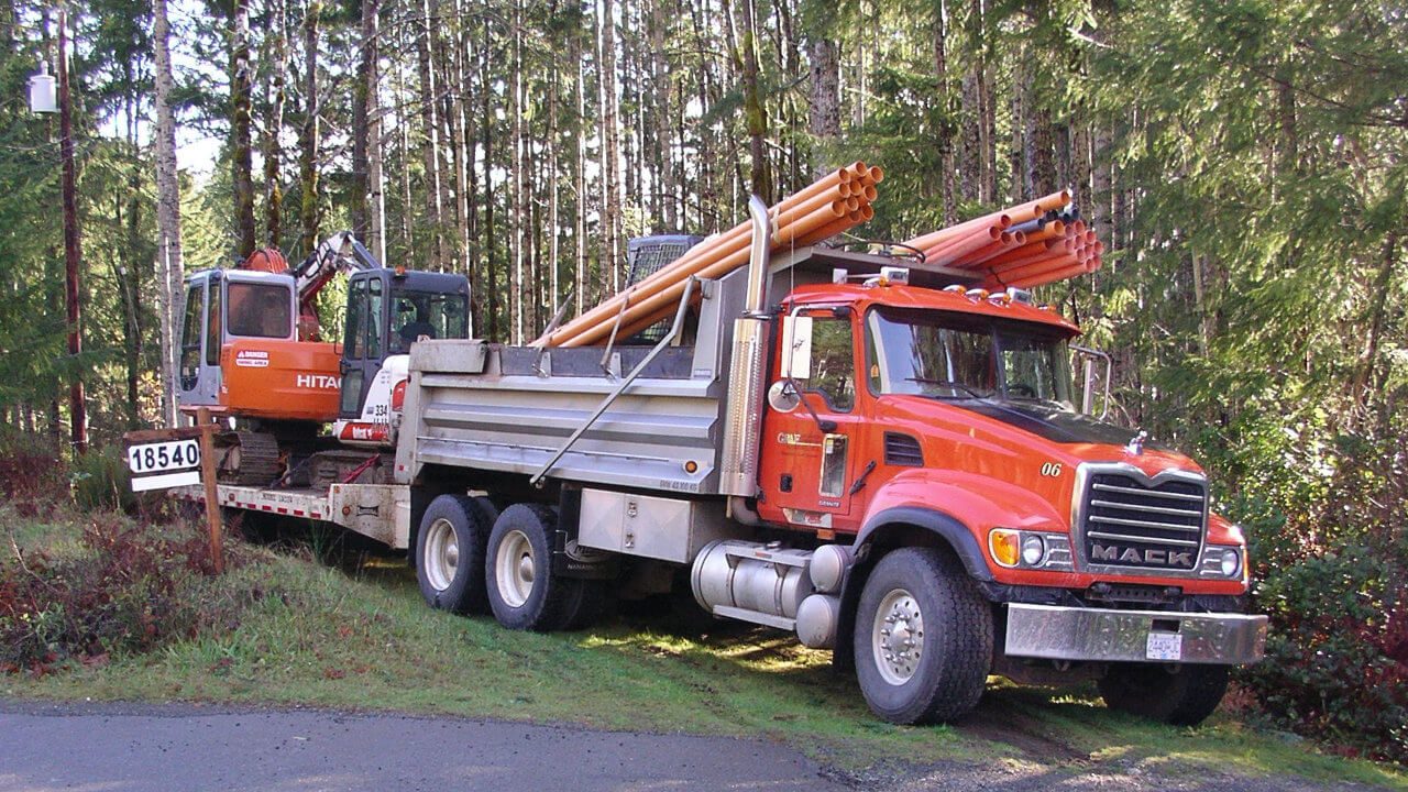 A red truck is parked next to a forest.